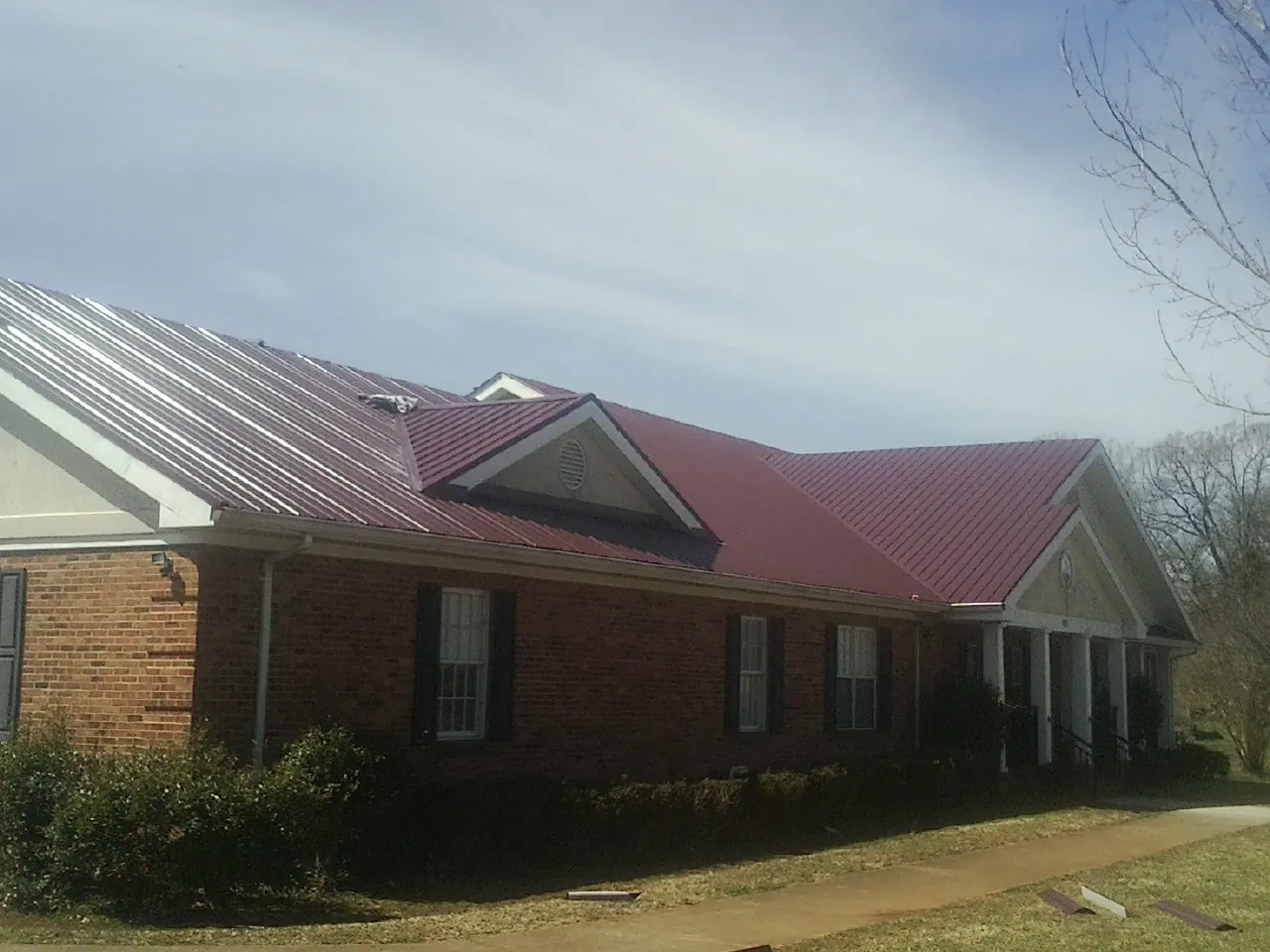 Red metal roof with gabled entries on a long brick building, from a Hail Damage Roof Repair job in Roebuck