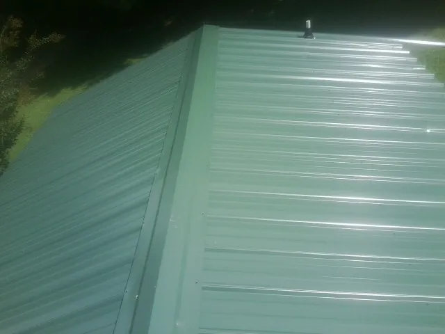 New green metal panels meeting at the ridge of a roof — Flat Roof Repair work by our crew in Roebuck