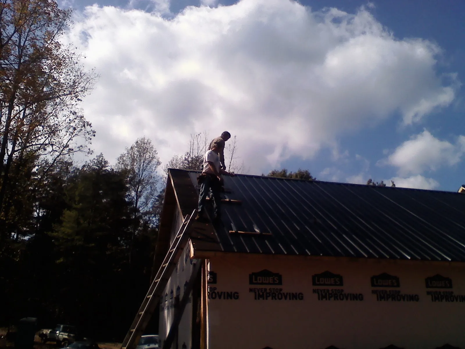Roofer fastening dark metal panels high against a cloudy sky, from a Roof Inspection job in Roebuck