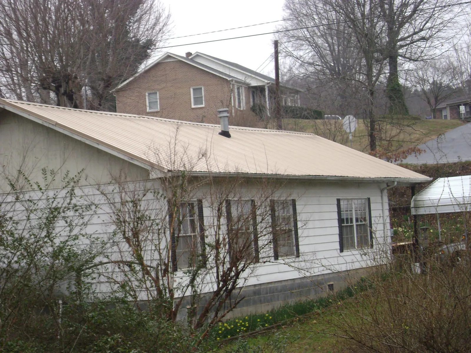 Tan metal roof on a white sided house set into a hillside — Commercial Roofing by Roofing Brothers in Roebuck