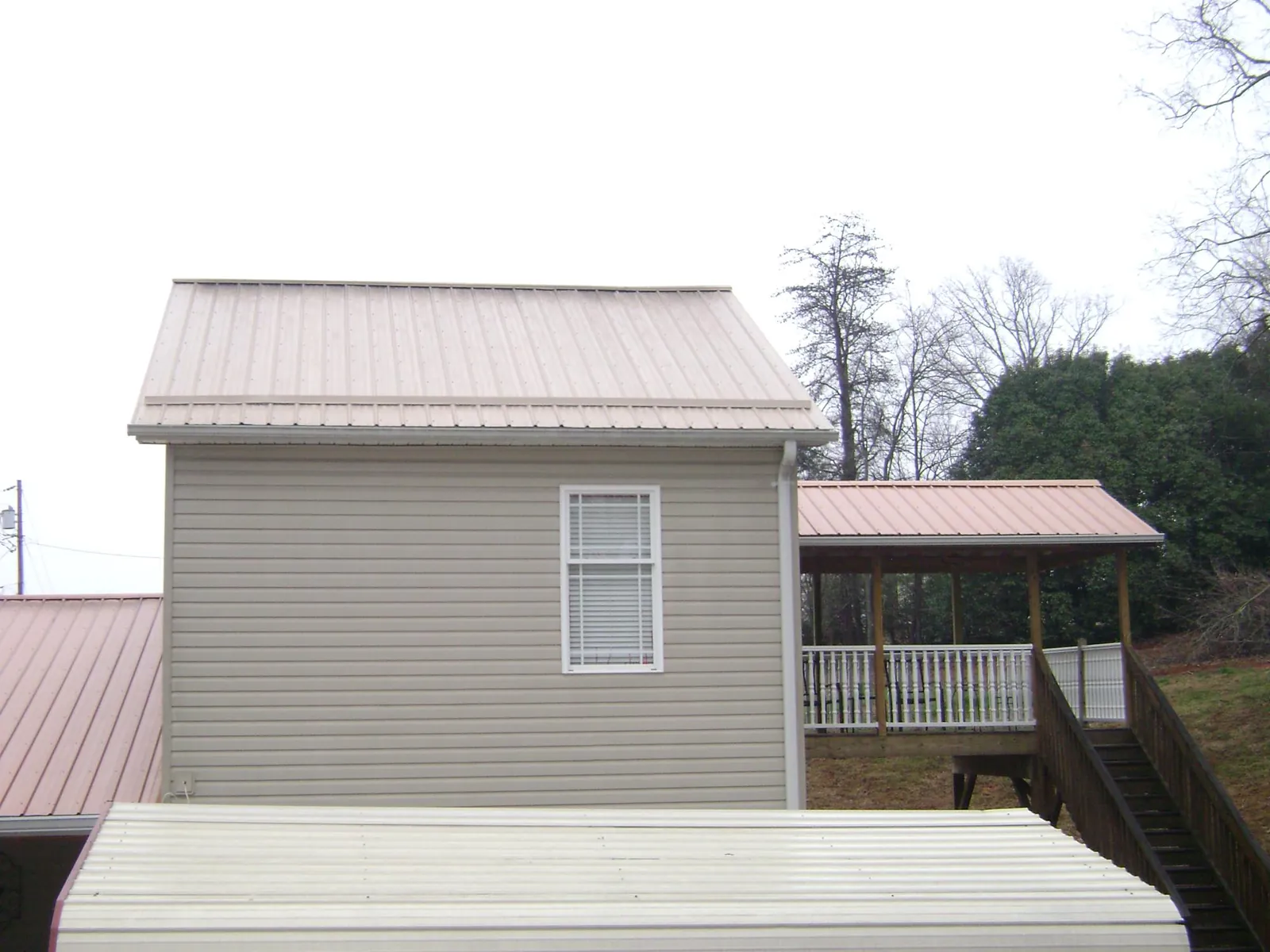 Tan metal roofs on a two story addition and attached porch, from a Roof Replacement job in Roebuck